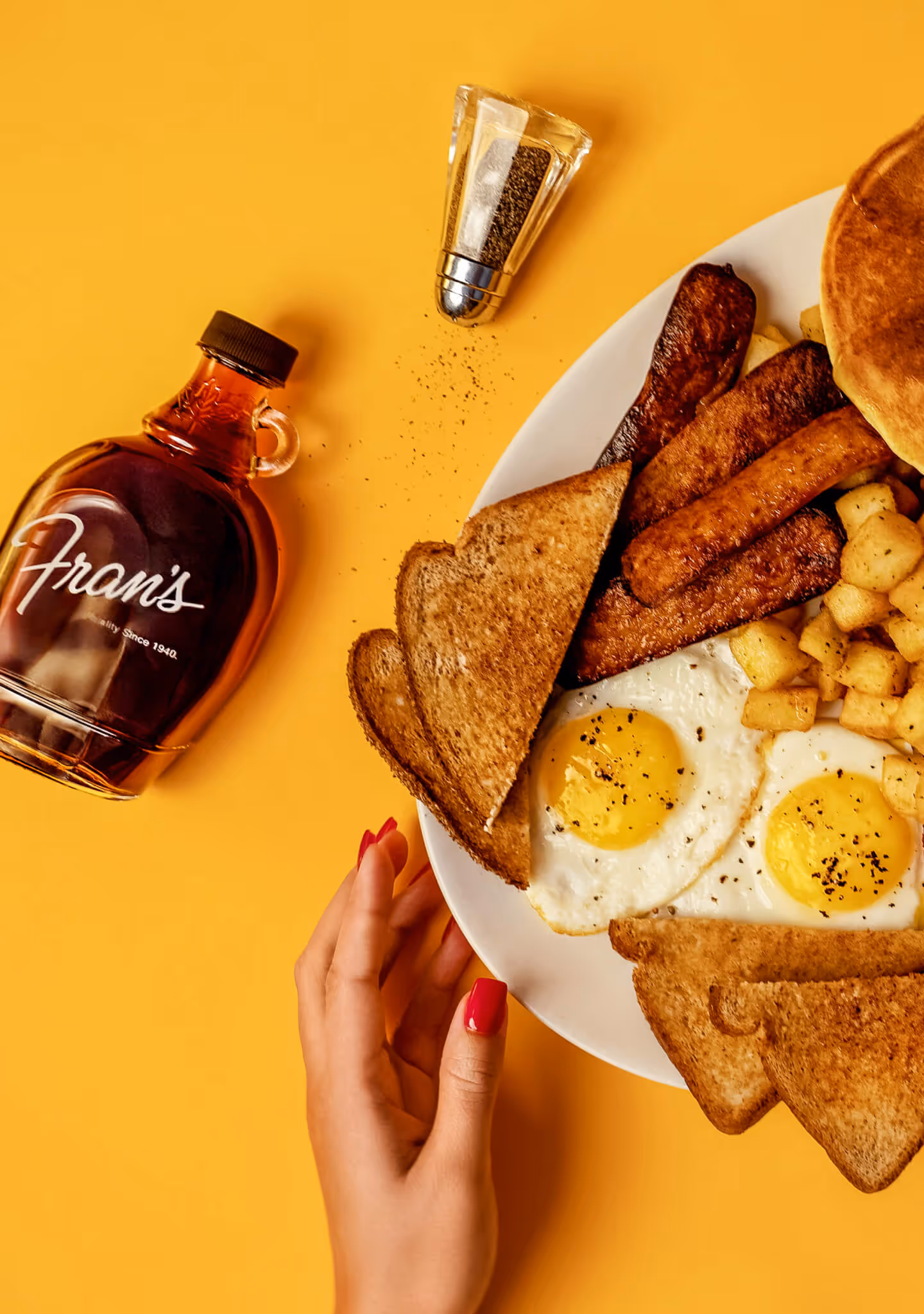 A big breakfast of eggs, bacon, sausages, toast and homefries beside a bottle of Fran's maple syrup