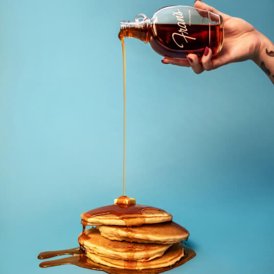 Maple syrup pouring from a Fran's bottle onto a stack of pancakes